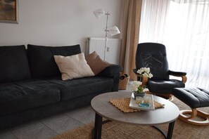A modern living room with a dark sofa, a round coffee table with a tray, a black leather chair, and a window with sheer curtains. - Kreyenschulte apartment (Borkum)