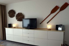 A flat-screen TV on a white cabinet with two wall-mounted decorative items and two wooden paddles. - Kreyenschulte apartment (Borkum)