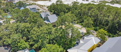 Vista aérea de uma área residencial costeira com casas, vegetação densa e uma praia.