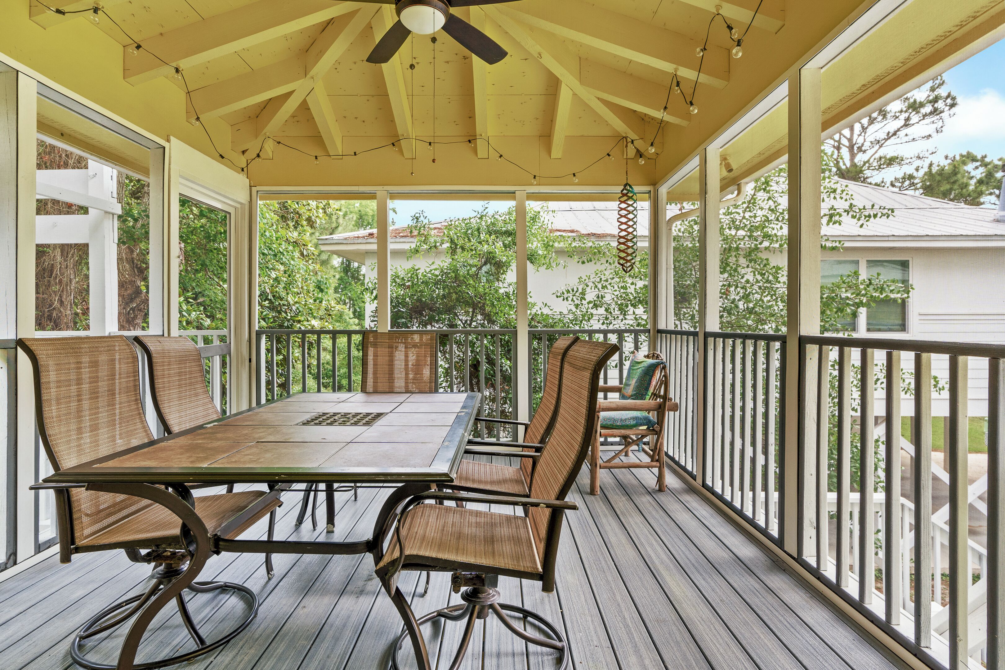 A covered patio with a table and chairs, wooden deck flooring, and a railing.