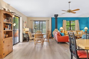 A spacious living room with a dining area, a fireplace, and large windows offering a view of the outdoors. - As You Like It | Steps to the Beach | Peek-a-boo Views (Santa Rosa Beach)
