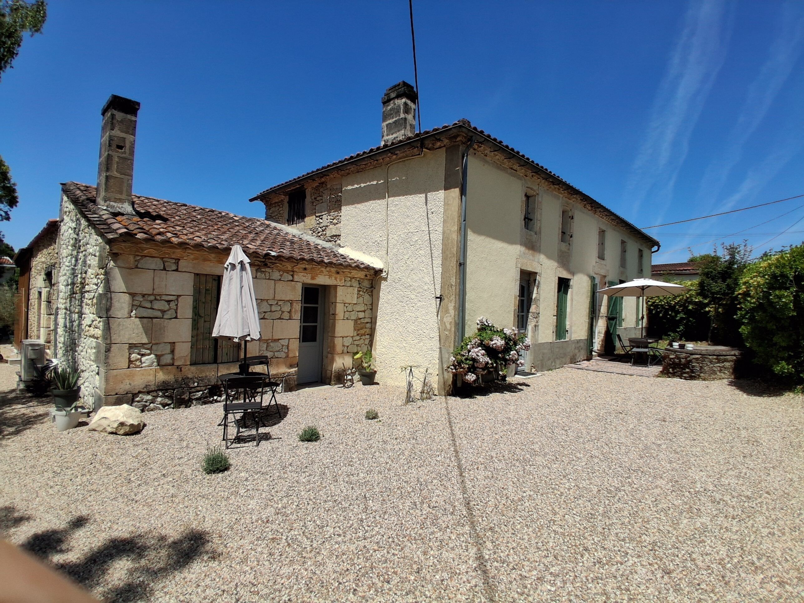A stone building with a tiled roof, a gravel courtyard, and outdoor seating.