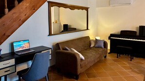 Ein Wohnzimmer mit Treppe, einem Sofa, einem Schreibtisch mit Laptop, einem Klavier und einem großen Spiegel.