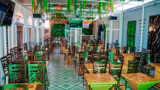 A restaurant with multiple tables and chairs, a tiled floor, and hanging plants. - NAAMIN SPORTS LOUNGE KAGIO (Kagio)