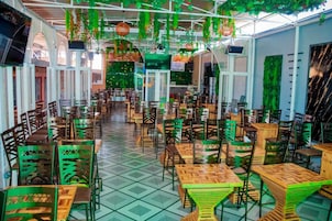 Un restaurante con varias mesas y sillas, suelo de baldosas y plantas colgantes.