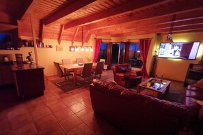 Ein gemütliches Wohnzimmer mit Holzboden, einer Essecke mit Tisch und Stühlen, einer Ledersofa und einem an der Wand befestigten Fernseher.