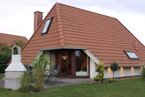 Ein Haus mit geneigtem Dach, einem Schornstein und einer kleinen Veranda mit Stühlen.