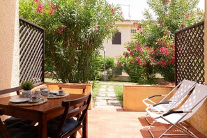 A patio with a table set for two, a pair of lounge chairs, and a garden with flowering plants. - Casa Pinta by Wonderful Italy (Arzachena)
