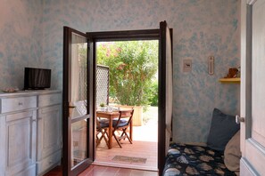 A room with a sliding glass door leading to an outdoor area with a table and chairs, a television on a cabinet, and a bed with patterned bedding. - Casa Pinta by Wonderful Italy (Arzachena)