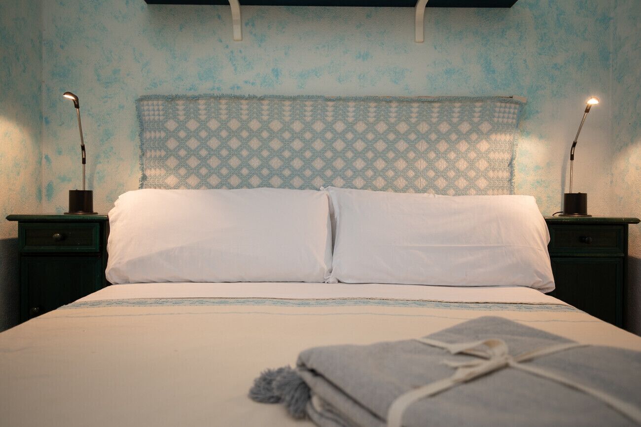 Un letto con lenzuola bianche, due comodini e una testiera decorata.