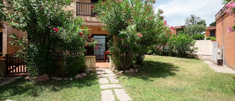 A residential building with a stone pathway leading to the entrance, surrounded by lush greenery and flowering plants.