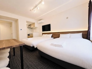 Ein Hotelzimmer mit zwei Betten, einem Schreibtisch, einem Flachbildfernseher und einer Klimaanlage.