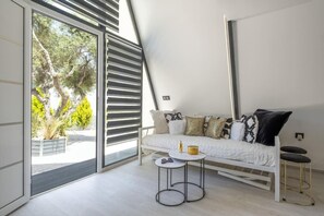 Ein modernes Zimmer mit einem Bett, einem kleinen runden Tisch und einem großen Fenster mit Jalousien.