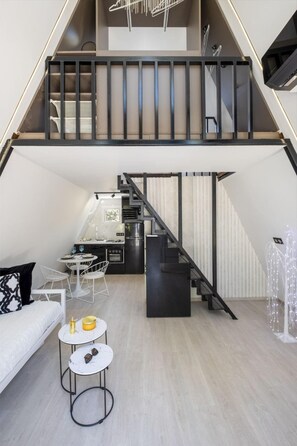 Eine Loft-Wohnung mit einer Wendeltreppe, die zwei Ebenen verbindet, einer Küchenzeile und einer Sitzecke mit einer Couch und kleinen Tischen.