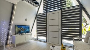 A modern bedroom with a sloped ceiling, a bed, a small table, a TV, and a wardrobe. - A truly distinctive retreat where contemporary design,natural beauty. (Chania)