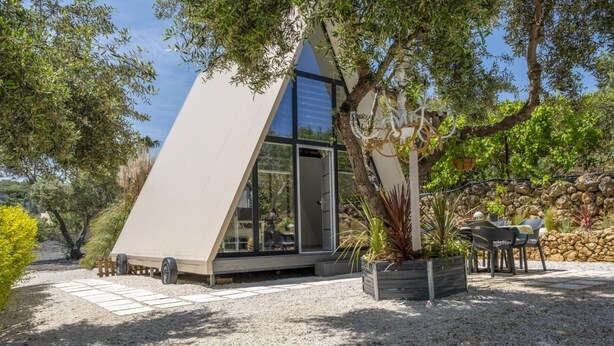 A modern, triangular-shaped building with a large glass door, surrounded by gravel and trees. - A truly distinctive retreat where contemporary design,natural beauty. (Chania)