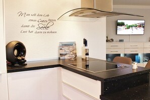 A modern kitchen with a black countertop, white cabinets, a built-in stove, and a wall-mounted TV. - More about the Wadden Sea Doris Frenzel (Cuxhaven)