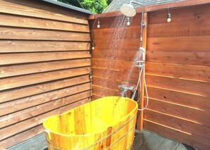 A wooden outdoor shower enclosure with a yellow tub.