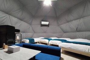 A compact, well-lit room with a sofa, two beds, a small table, and a microwave.