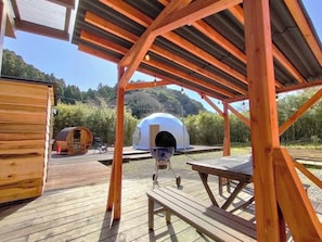 A wooden deck with a covered seating area, a wooden barrel, and a dome-shaped structure.