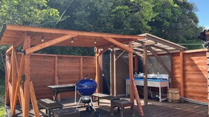 A wooden outdoor structure with a barbecue grill, a sink, and a table.