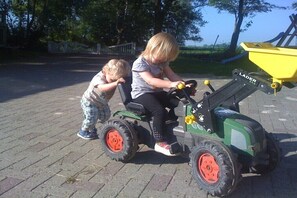 Two children riding a green toy tractor on a paved surface. - 3 on the farm of Wattenmeer Ferien (Butjadingen)