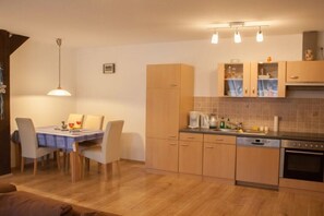 A compact kitchen with wooden cabinets, a dining area with a table and chairs, and a modern pendant light. - 3 on the farm of Wattenmeer Ferien (Butjadingen)