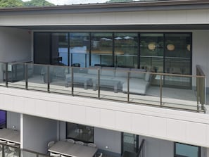 Un bâtiment moderne à deux étages, doté d’un balcon en verre, d’un espace extérieur aménagé et offrant une vue sur une étendue d’eau.