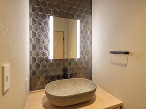 Une salle de bain avec un lavabo en pierre de forme ronde, un miroir et un pare-chocs en carreaux hexagonaux.