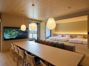 Ein modernes Hotelzimmer mit einem großen Bett, einer Essecke mit Tisch und Stühlen sowie einem Fernseher, der eine Naturansicht zeigt.