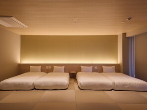 Ein Hotelzimmer mit zwei Betten, einem großen Wand-Fernseher und einer Decke mit Einbaustrahlern.