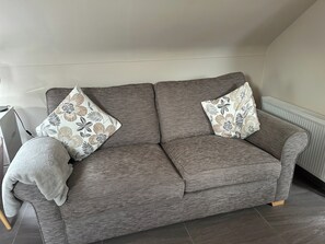 A grey sofa with floral-patterned cushions in a room with a radiator and a tiled floor. - Omagh Studio b&b With Light Breakfast Inc (Omagh)