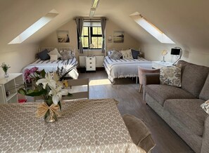 A cozy attic bedroom with two beds, a sofa, a table, and a vase of flowers. - Omagh Studio b&b With Light Breakfast Inc (Omagh)