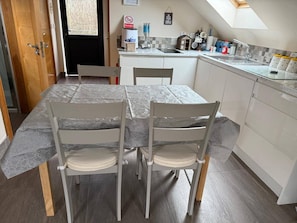 A dining area with a table covered in a protective sheet, two chairs, and a kitchen in the background. - Omagh Studio b&b With Light Breakfast Inc (Omagh)
