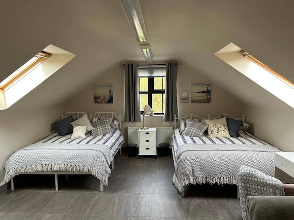 A bedroom with two beds, a nightstand, a window with curtains, and a radiator. - Omagh Studio b&b With Light Breakfast Inc (Omagh)