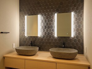 Une salle de bain avec deux vasques sur pied, un mur orné d’un motif hexagonal et un meuble-lavabo en bois.