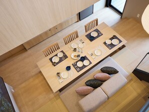 Un coin repas avec une table en bois dressée pour quatre personnes, un canapé avec des coussins et une vue sur l’extérieur.