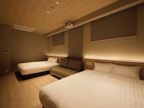 Une chambre d’hôtel avec deux lits, un canapé, des spots encastrés au plafond et un projecteur fixé au mur.
