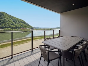 Un balcon avec une table et des chaises donnant sur un lac et des collines.