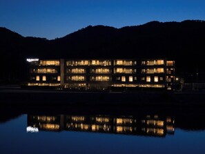 Un hôtel à plusieurs étages dont l’image se reflète dans l’eau, doté de balcons et d’une enseigne indiquant « Rakuten STAY ».