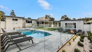 A modern pool area with a glass-enclosed deck, lounge chairs, and a fire feature. - Samphire House - Fireplace with Heated Swimming Pool (Callala Bay)