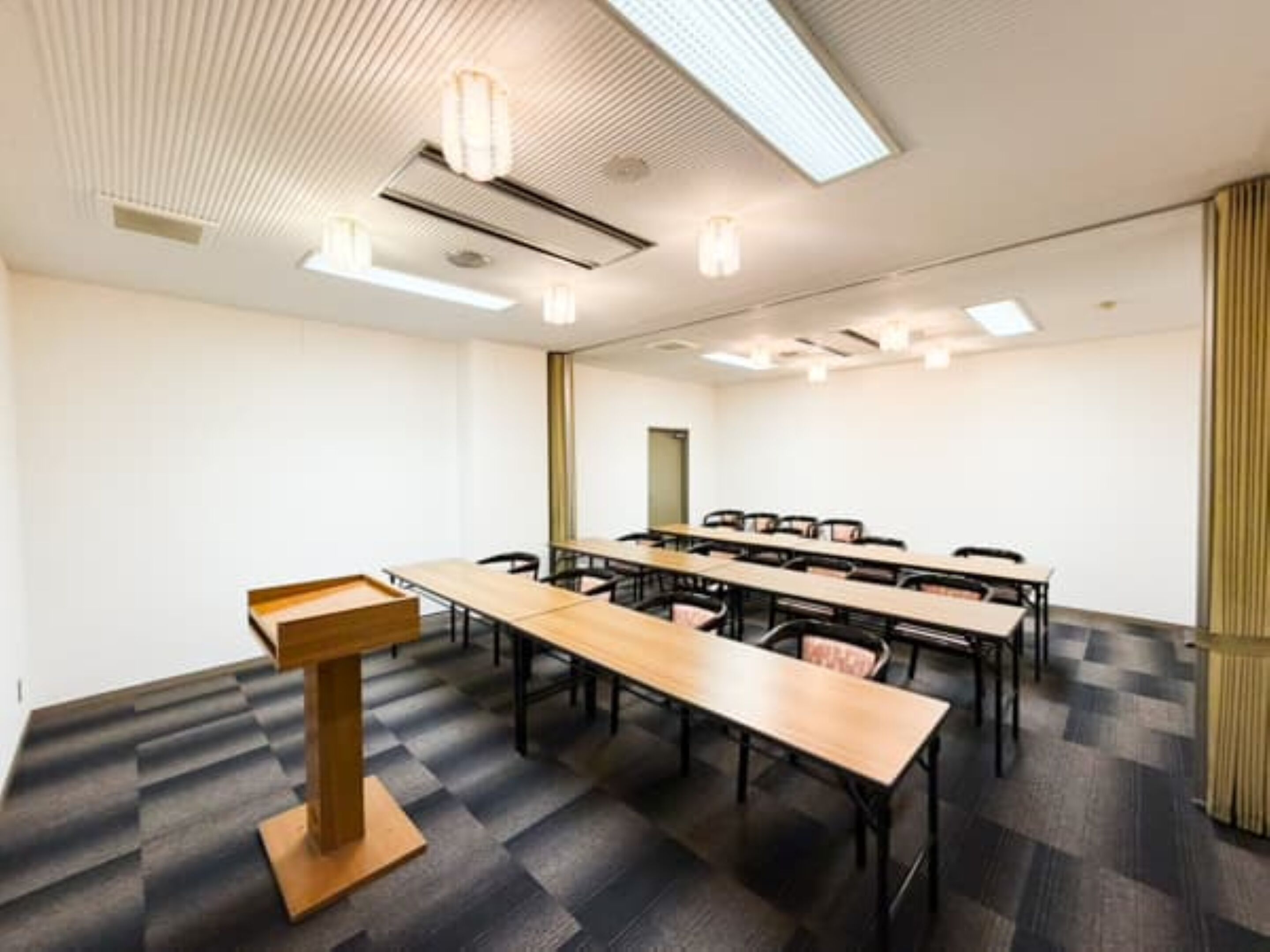 A conference room with a long table, chairs, a podium, and ceiling lights.