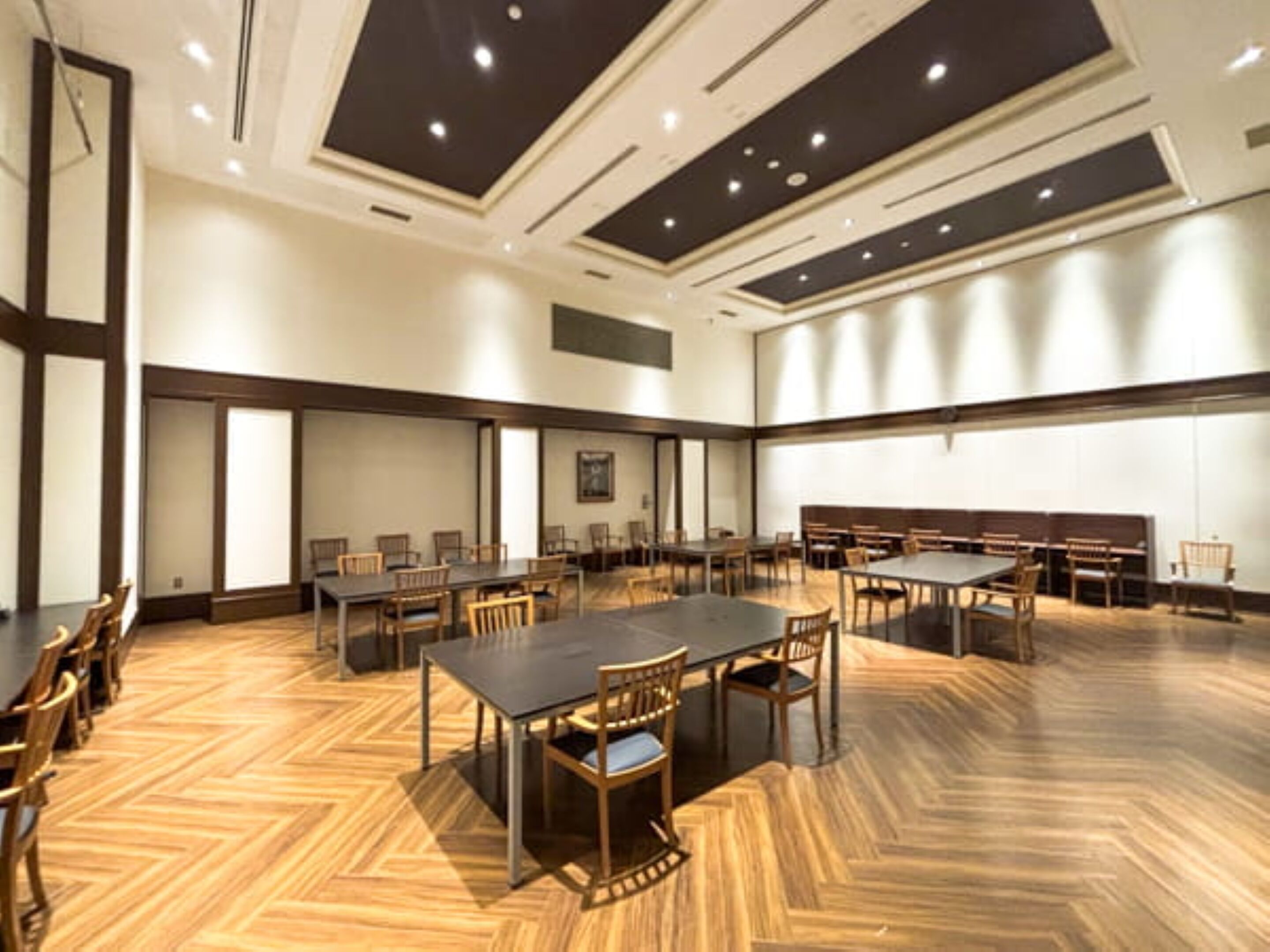 Un salón de conferencias con varias mesas y sillas, suelo de madera e iluminación empotrada en el techo.