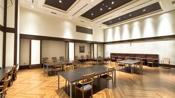 Un salón de conferencias con varias mesas y sillas, suelo de madera e iluminación empotrada en el techo.