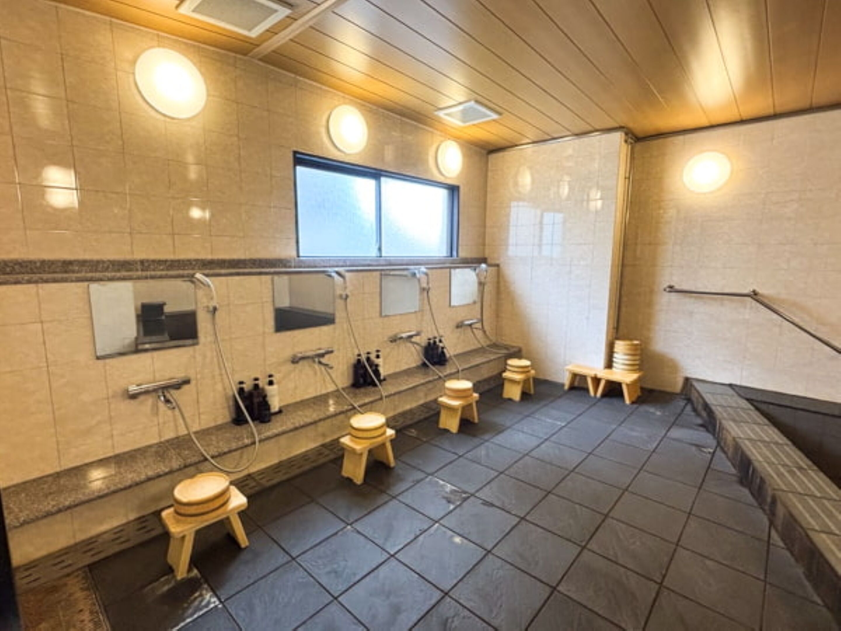 Baño público con varios lavamanos, espejos y taburetes.