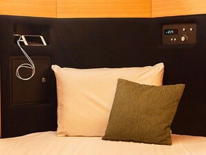 A bed with a white pillow and a green pillow, a control panel with a digital display, and a cable connected to a device on the wall. - HOTEL LiVEMAX Tottori GRANDE (Tottori-shi)