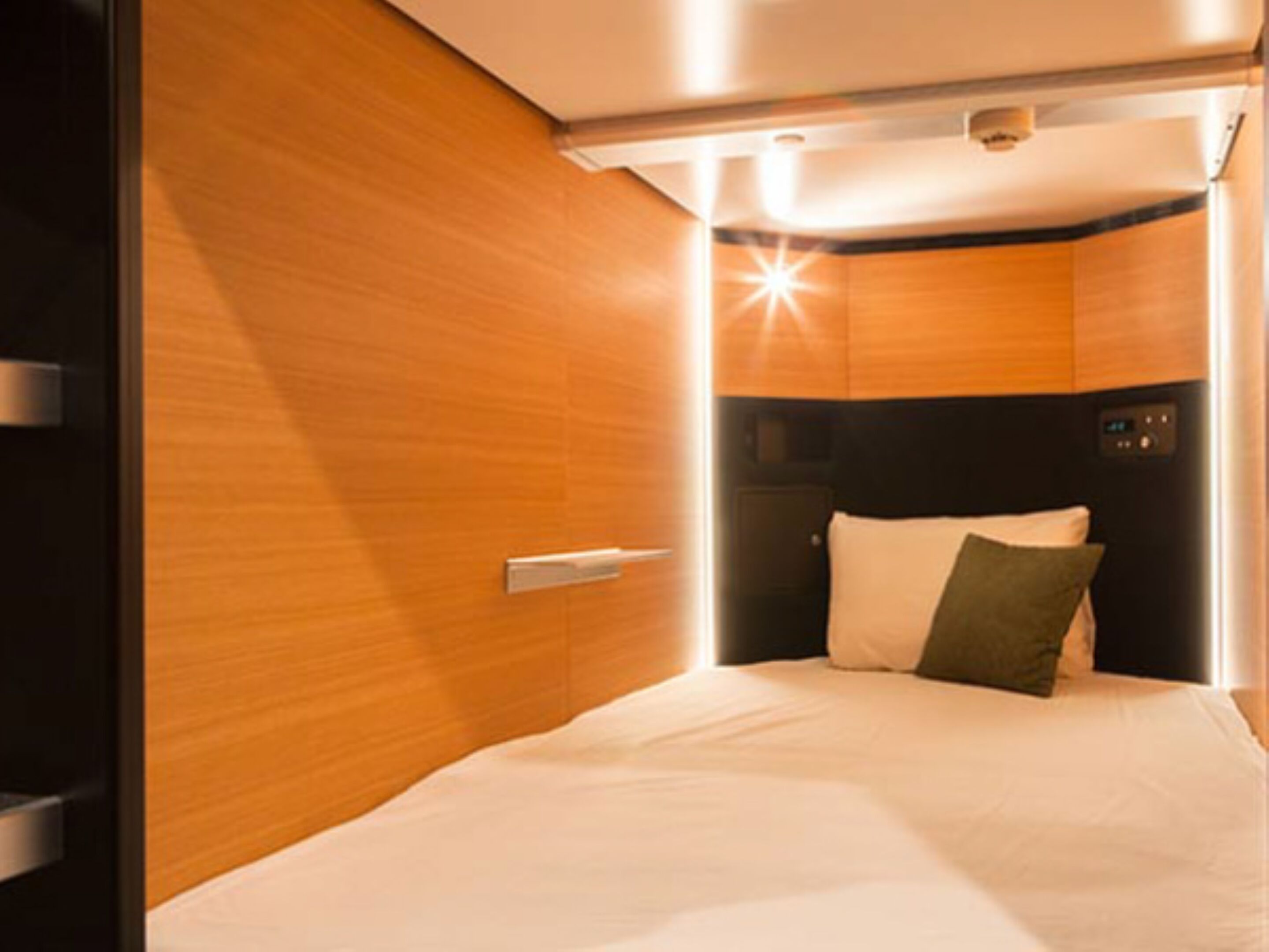 A compact, modern room with a bed, a control panel, and a wooden wall.