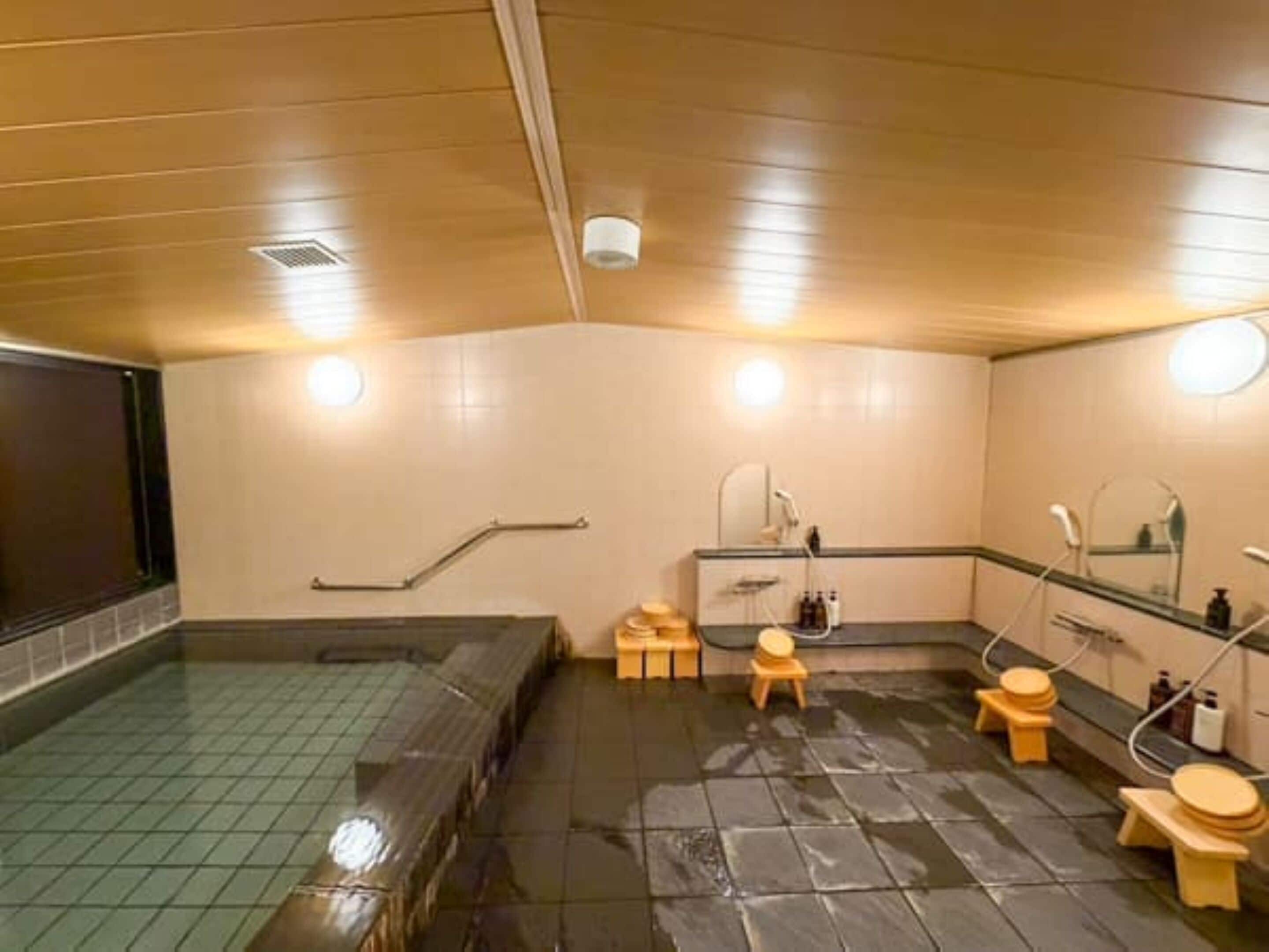 Un onsen japonais traditionnel, avec un sol en bois, un petit banc en bois, une baignoire et des toilettes.