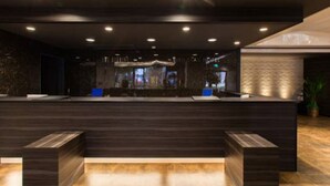 A reception desk with a dark wood finish, a stone wall, and recessed ceiling lighting. - HOTEL LiVEMAX Tottori GRANDE (Tottori)