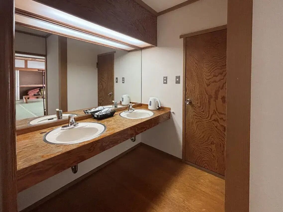 Une salle de bain avec deux lavabos, un miroir et une porte en bois.